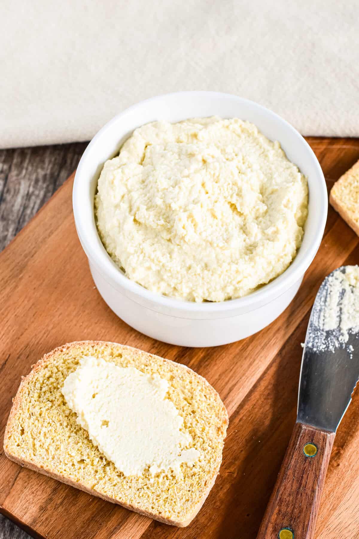 A piece of toast with a schmear of vegan ricotta on a wooden board.