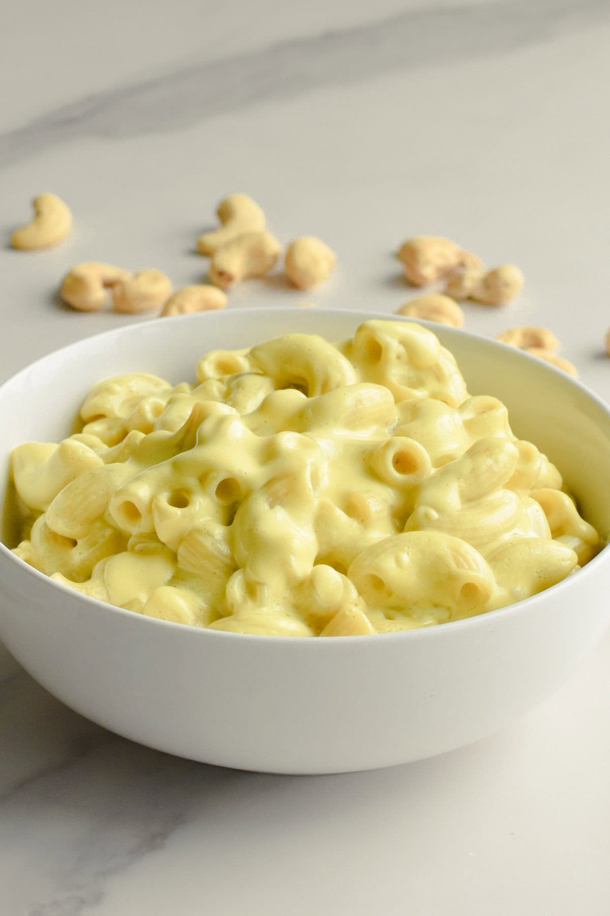 Cashew mac and cheese in a white bowl on a marble surface with cashews in the background.