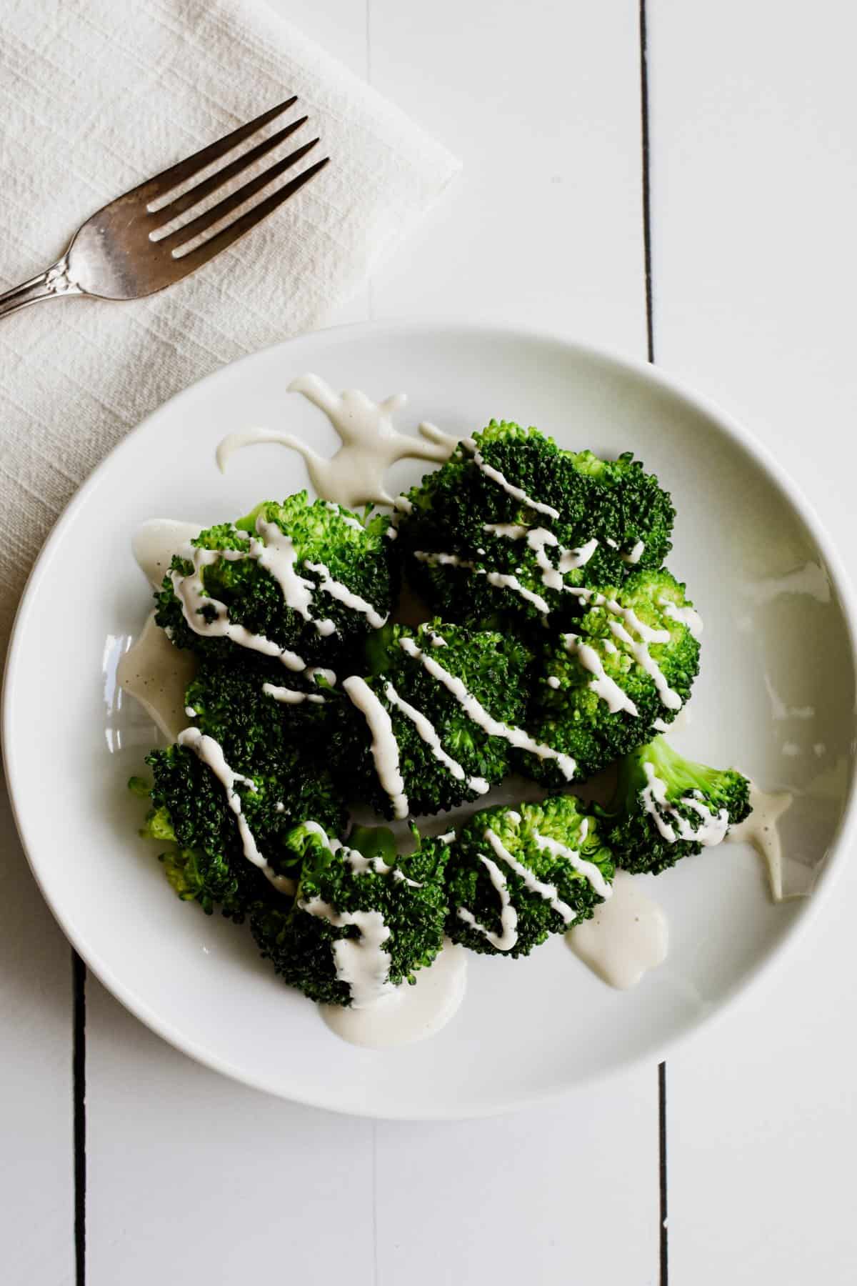 A white plate with a serving of steamed broccoli and cashew mozzarella sauce.