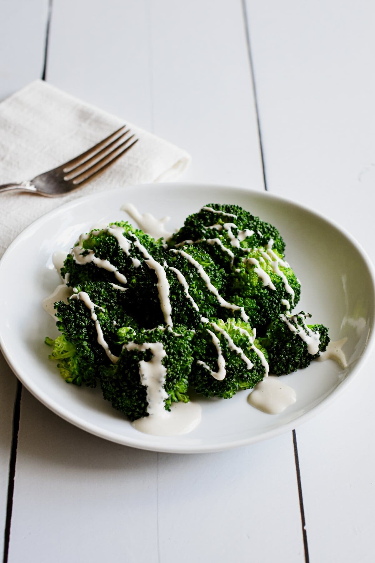 Steamed broccoli on a white plate with cashew cheese sauce.