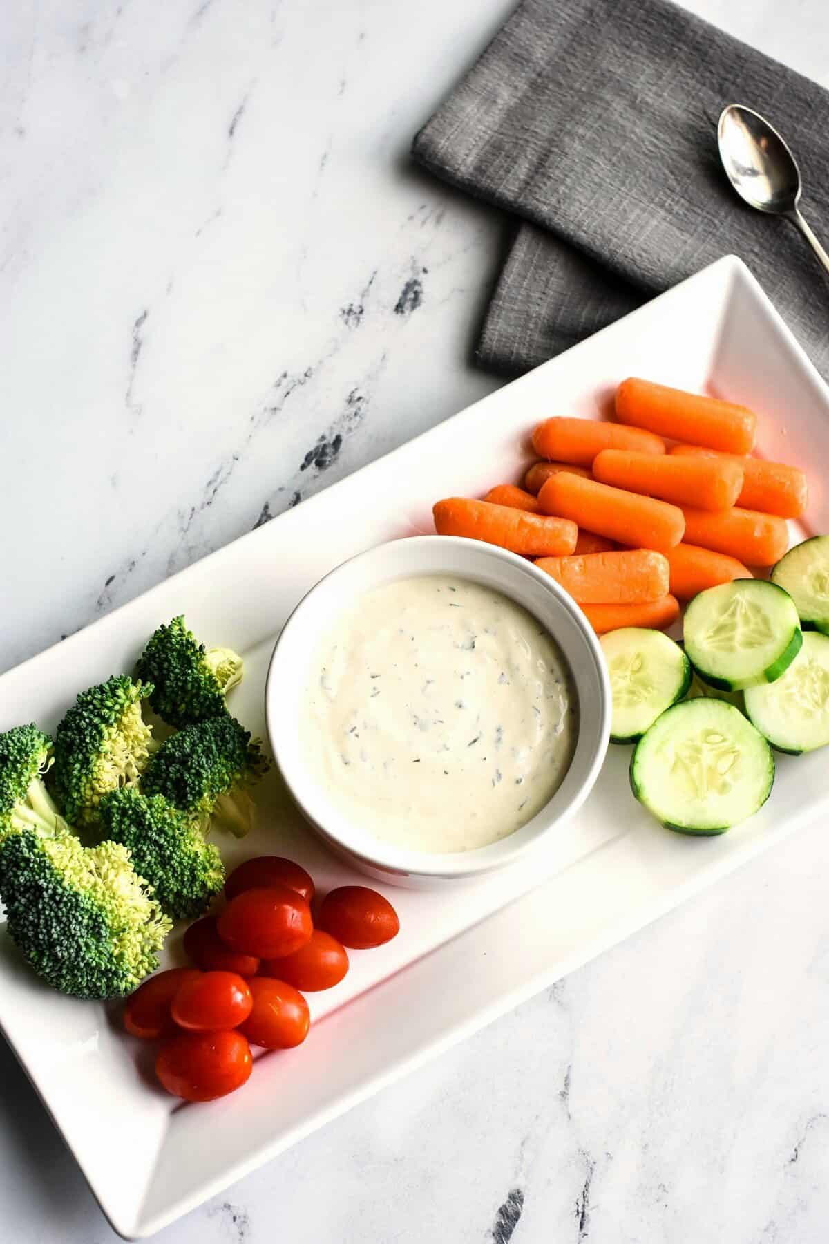 A veggie platter with a white bowl of ranch dressing in the middle.