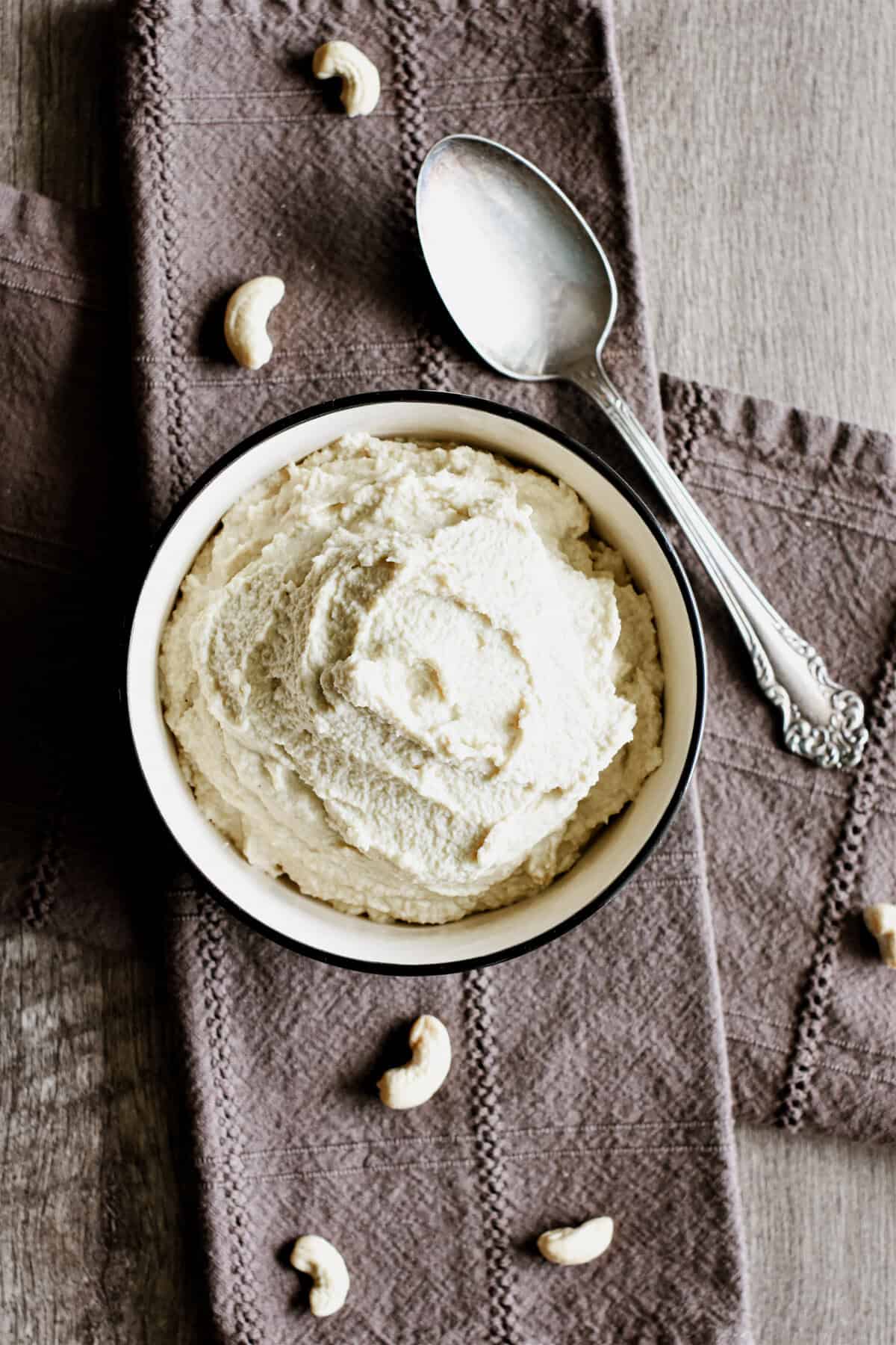 Vegan ricotta in a bowl on a kitchen napkin with cashews on it and a spoon.