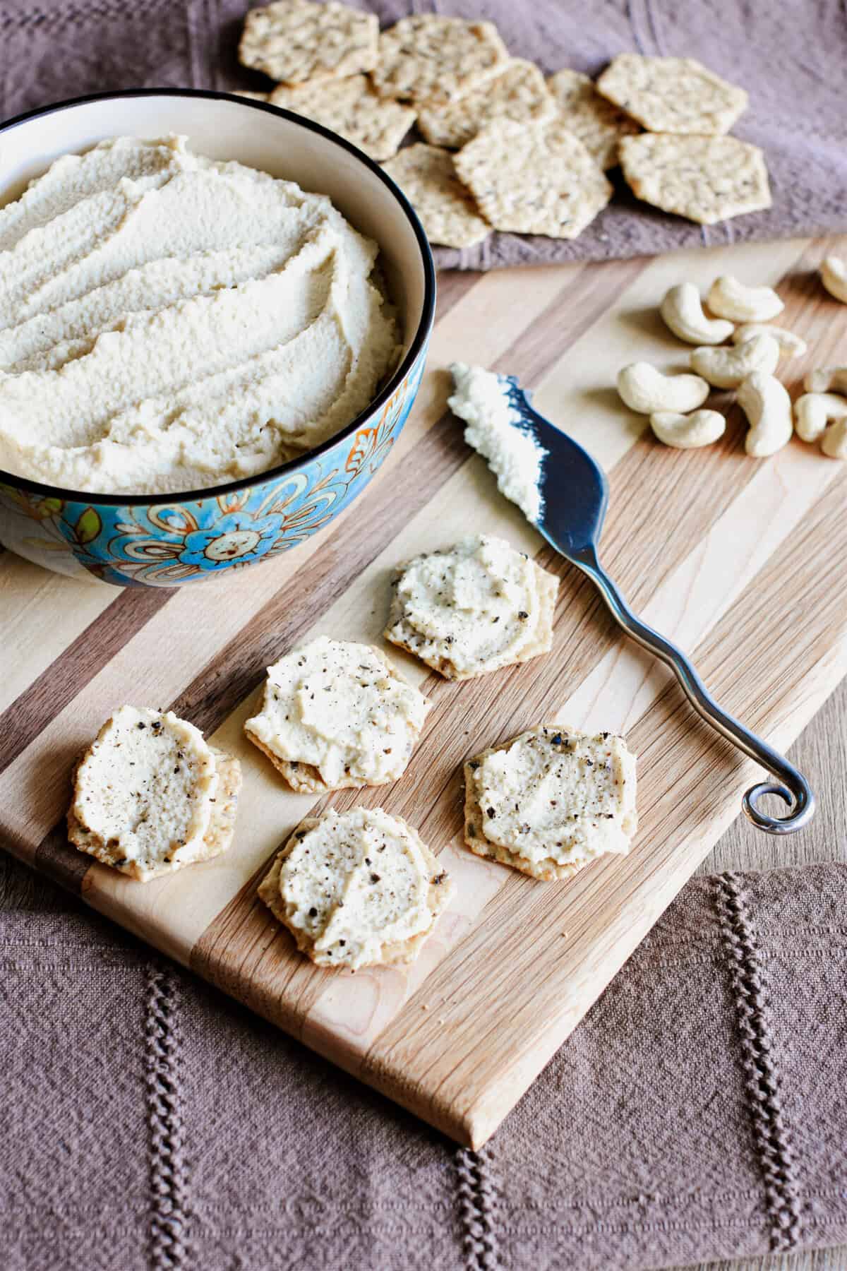 Cashew ricotta cheese in a bowl and some on crackers on a wooden board.
