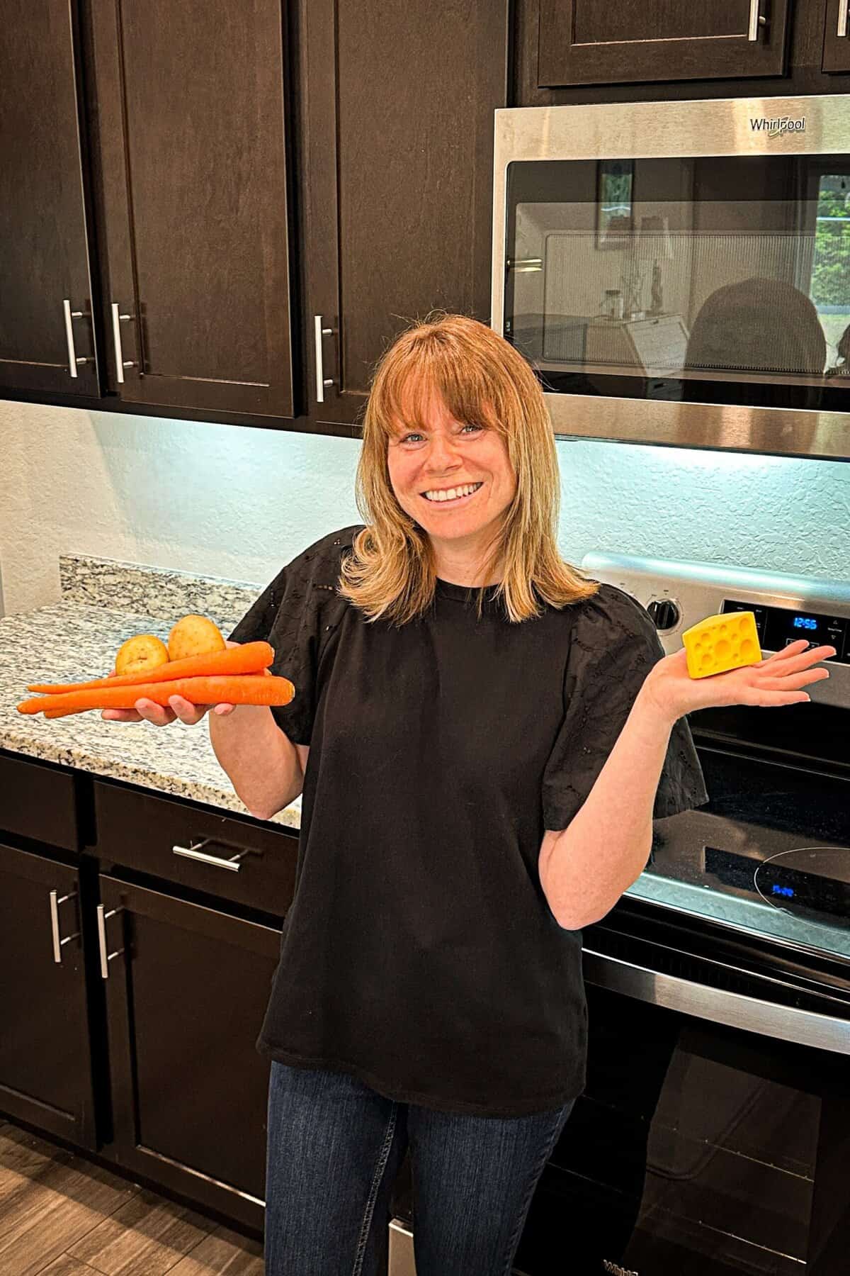 Author standing in front of an oven holding a fake piece of cheese in one hand and veggies in the other.