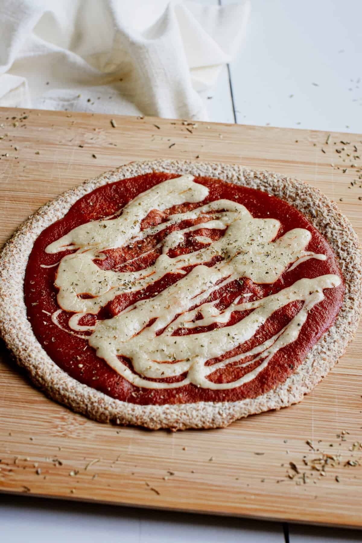 A tortilla pizza on a wooden board with sauce and vegan cheese on top.