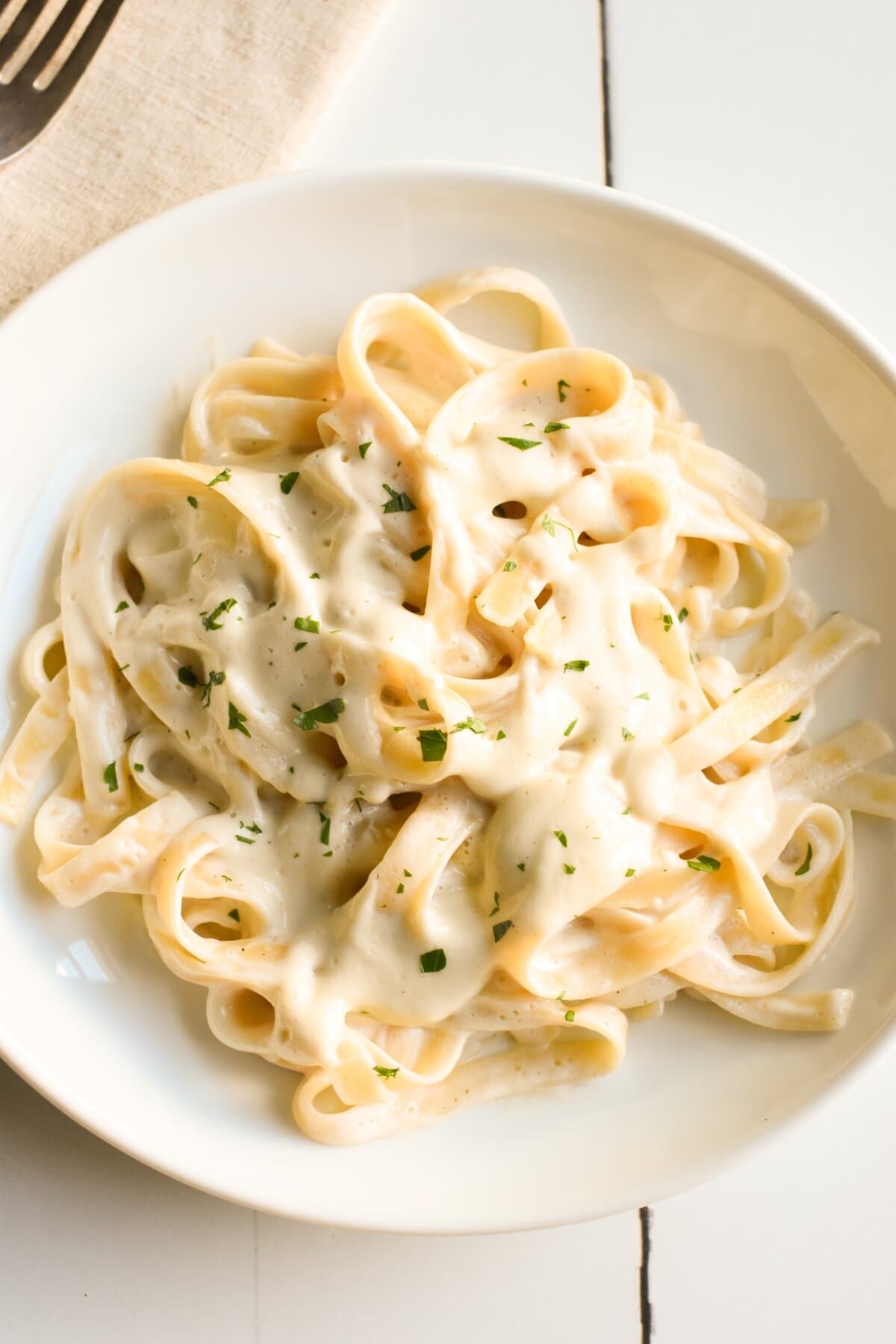 A white plate with vegan fettuccini alfredo on it, garnished with parsley.
