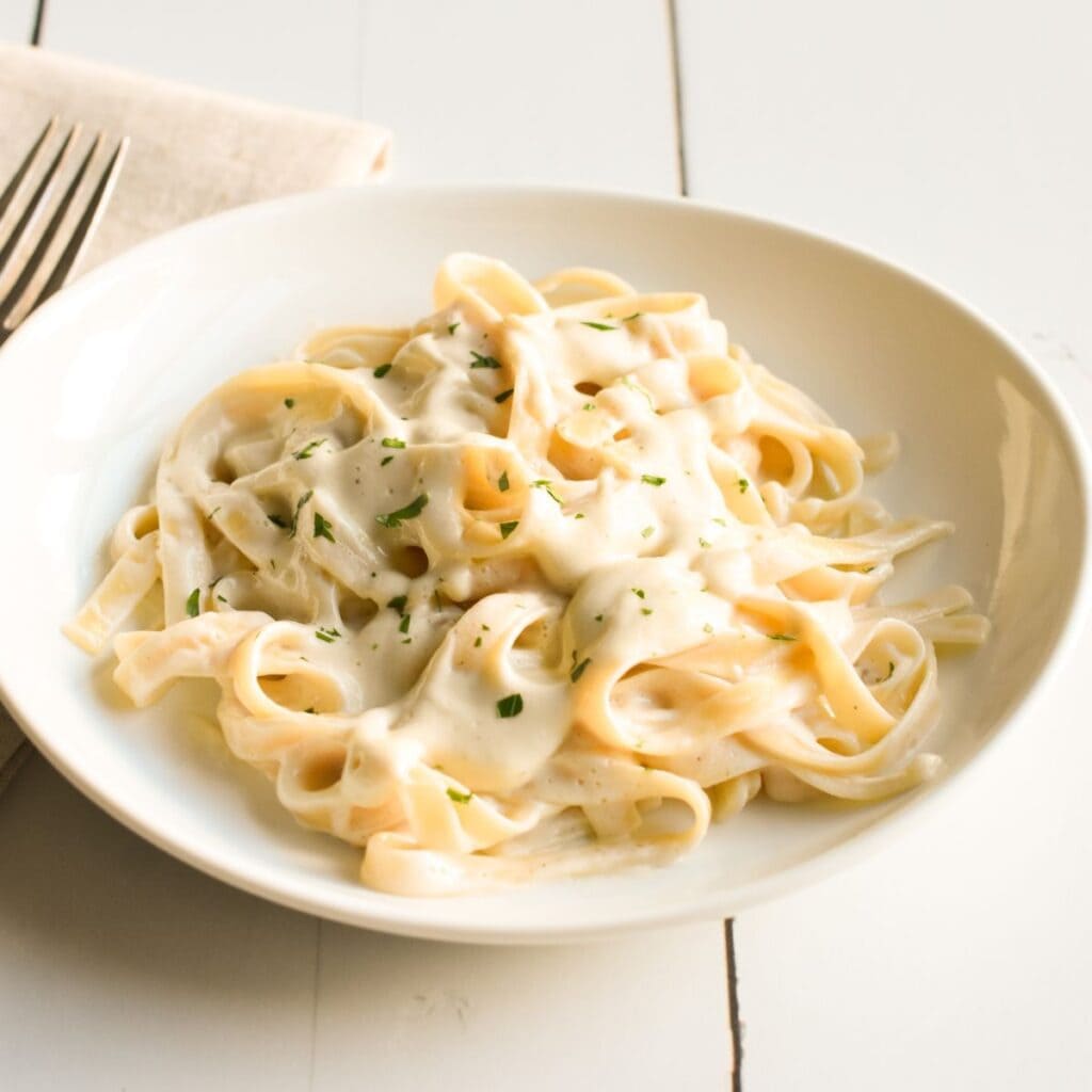 Dairy-free fettuccine alfredo on a white plate with fresh parsley on top.