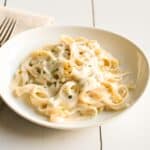 Dairy-free fettuccine alfredo on a white plate with fresh parsley on top.