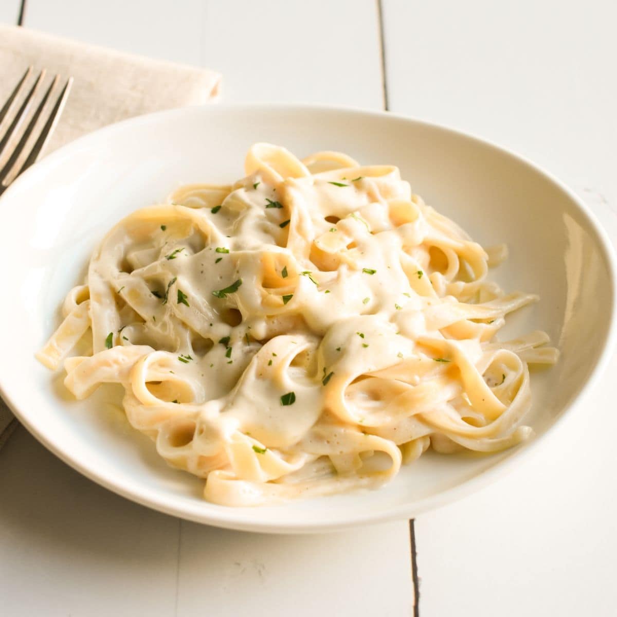 Dairy-free fettuccine alfredo on a white plate with fresh parsley on top.