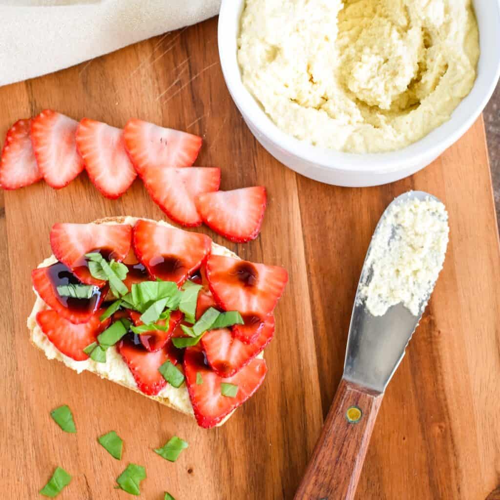 A slice of vegan ricotta toast with strawberries, balsamic, and basil on a wooden board.