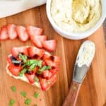 A slice of vegan ricotta toast with strawberries, balsamic, and basil on a wooden board.