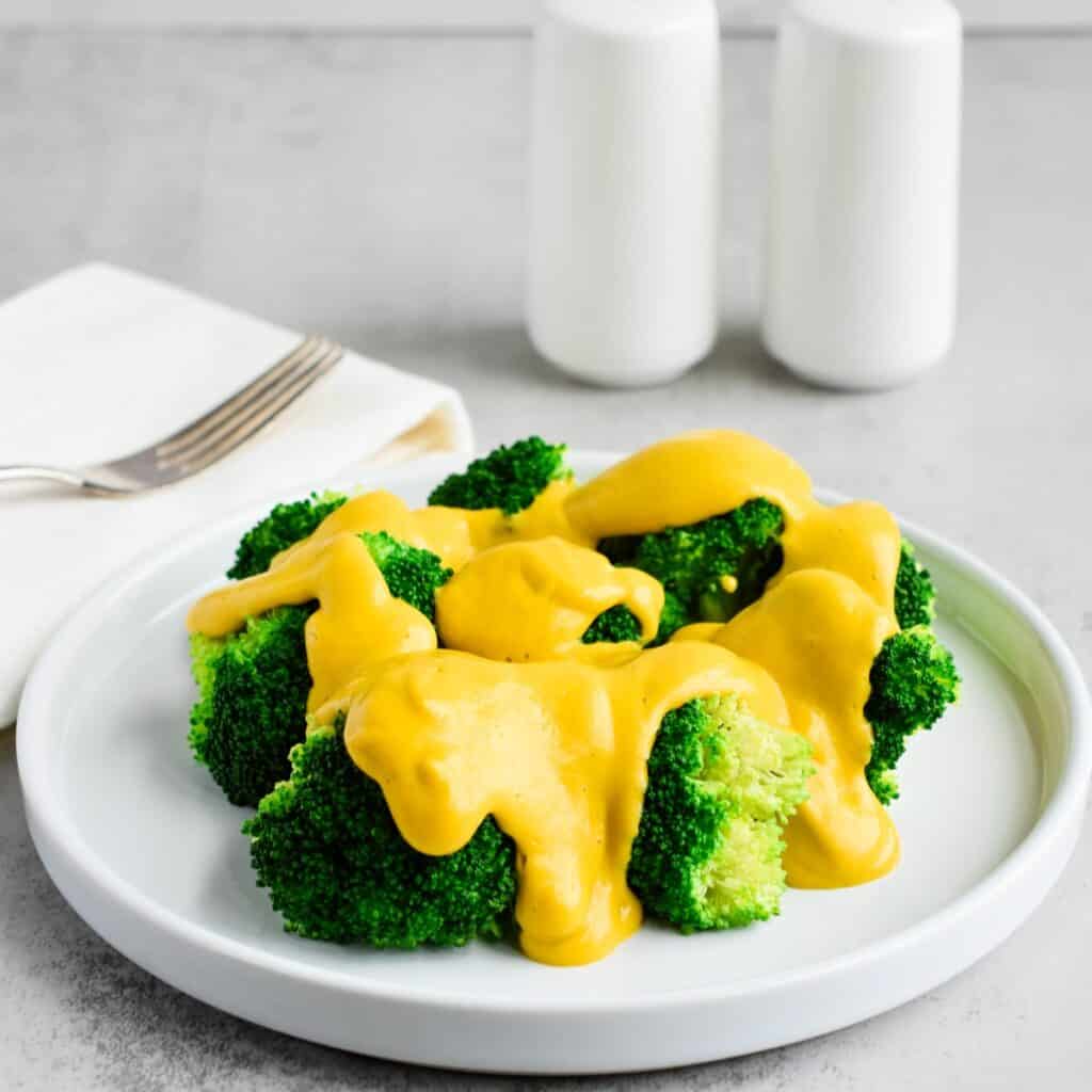 A white plate filled with broccoli and dairy-free cheese sauce.