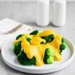 A white plate filled with broccoli and dairy-free cheese sauce.