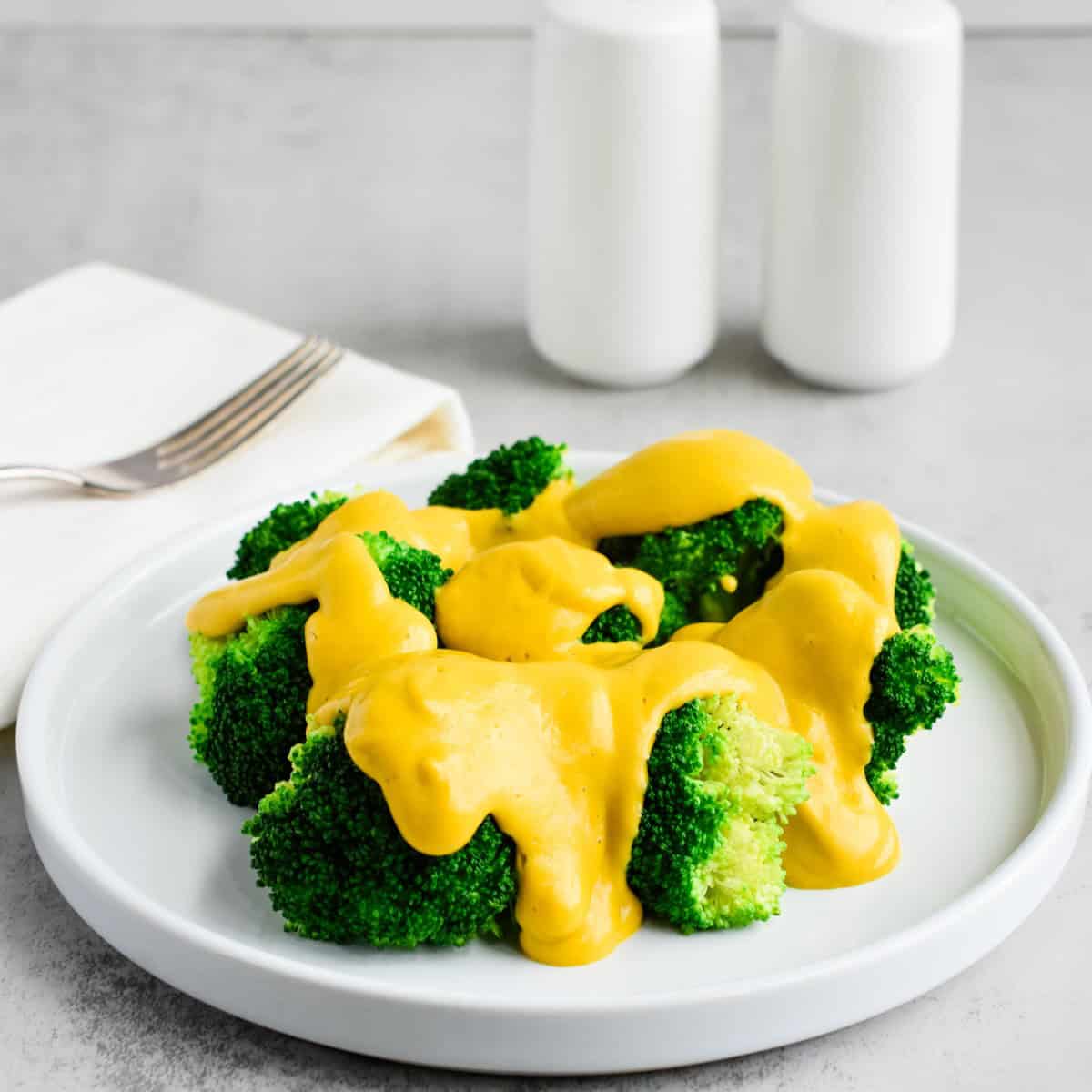 A white plate filled with broccoli and dairy-free cheese sauce.